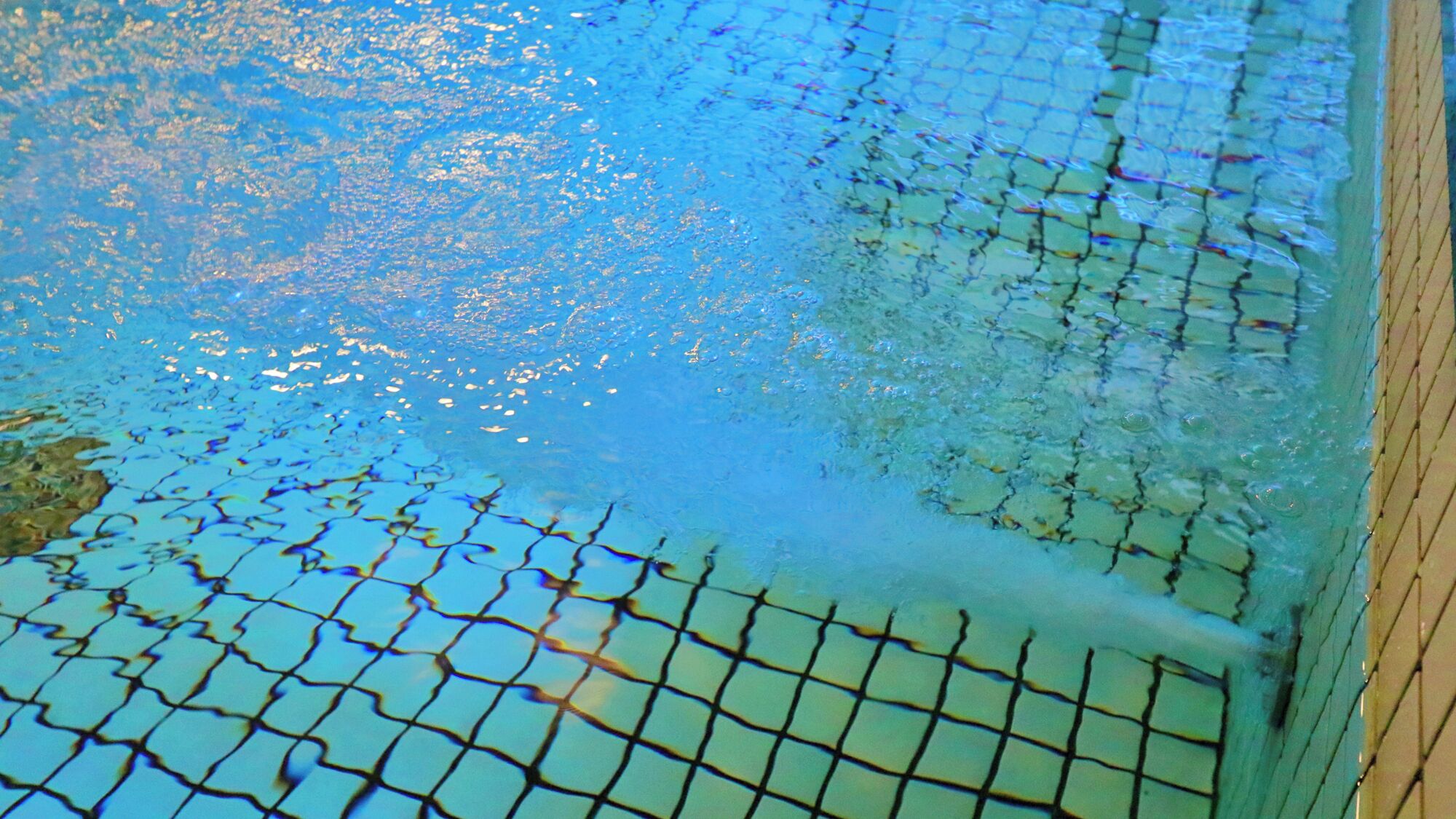 Une piscine dont le fond est recouvert d’un motif en damier, entourée d’une terrasse en bois.