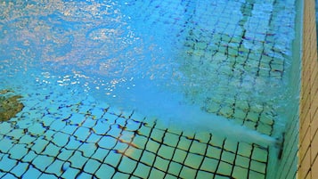 Une piscine dont le fond est recouvert d’un motif en damier, entourée d’une terrasse en bois.