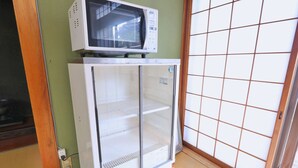 Un petit réfrigérateur blanc, surmonté d’un four à micro-ondes, se trouve dans une pièce dont un des murs est vert et qui est dotée d’une porte coulissante de type shoji.
