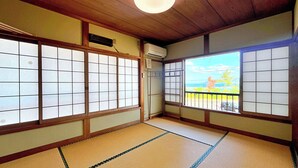 Une pièce de style japonais traditionnel, avec un sol recouvert de tatamis, des paravents en papier de riz (shoji) et une vue sur un parking et des arbres.