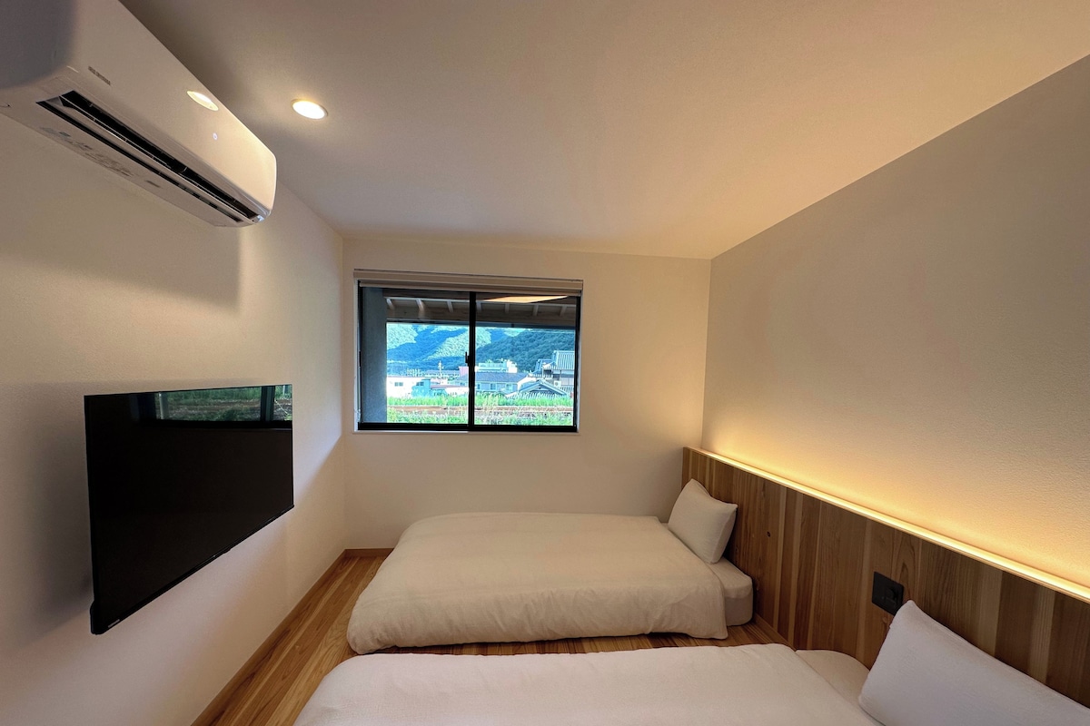 A hotel room with two beds, a TV, an air conditioner, and a window with a view of a landscape.
