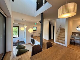 Un interior moderno con una mesa de comedor de madera, una escalera e iluminación colgante.