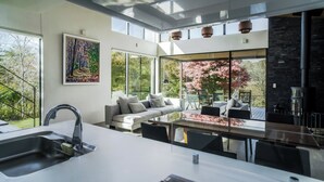 A modern kitchen with a large island, a dining area with a glass table, and a sofa. - Sukh (Karuizawa)