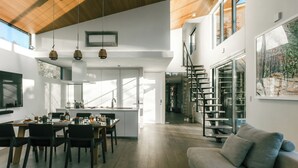 A spacious kitchen with a dining area, a staircase, and a large window. - Sukh (Karuizawa)
