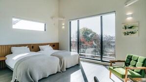 A modern hotel room with two beds, large windows, a green armchair, and a view of trees. - Sukh (Karuizawa)
