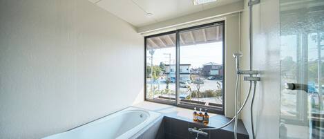 A modern bathroom with a bathtub, a shower, and a window with a view of the street.