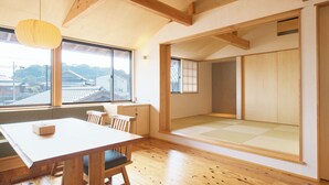 A traditional Japanese room with tatami flooring, a wooden table with chairs, a sliding shoji screen, and a view of traditional buildings outside. - Kiminoya (Awaji)