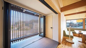 A modern interior with a sliding glass door leading to a balcony, a wooden floor, and a view of traditional buildings outside. - Kiminoya (Awaji)