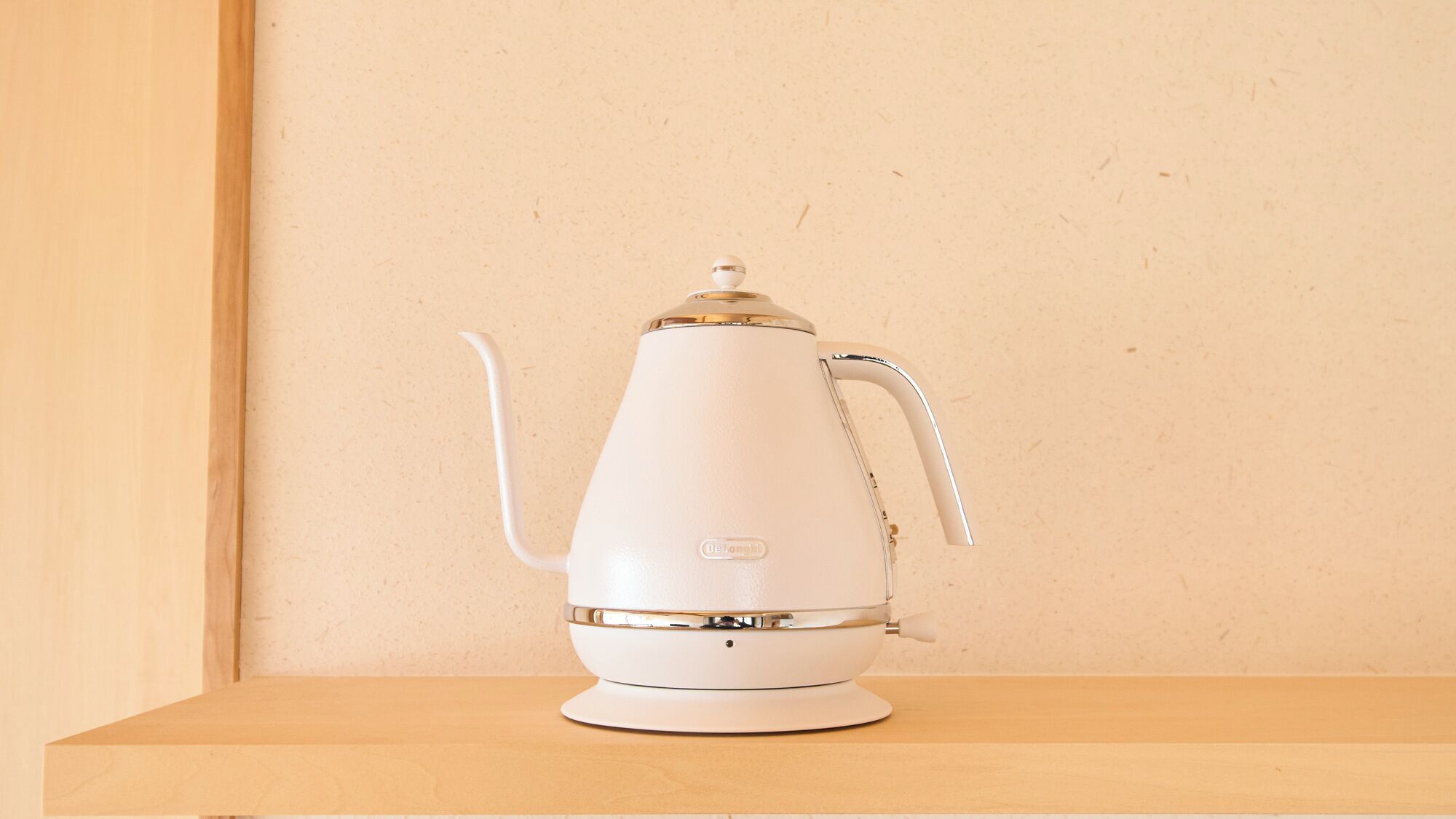 A white electric kettle on a wooden shelf against a plain wall.