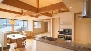 A modern kitchen with wooden beams, a dining area with a table and chairs, and a view of the outside through large windows. - Kiminoya (Awaji)
