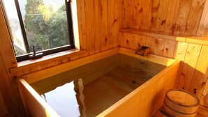A wooden cabin with a large wooden bathtub, a window, and a wooden bench. - Mutsumian (Kawazu)