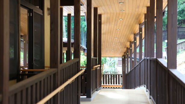 A covered walkway with wooden railings and a view of greenery outside. - Mutsumian (Kawazu)