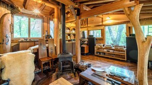 A rustic cabin interior with a fireplace, wooden beams, and large windows. - Log Cottage Chausu no Mori (Nasu)