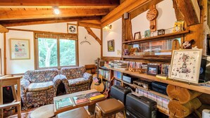 A cozy room with wooden beams, a sofa, a coffee table, a bookshelf, and a window with a view of trees. - Log Cottage Chausu no Mori (Nasu)