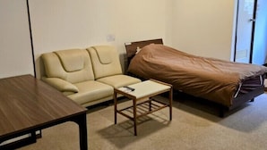 A small, sparsely furnished room with a bed, a sofa, a small table, and a wooden bench. - Business Hotel Nishiwaki (Nishiwaki)
