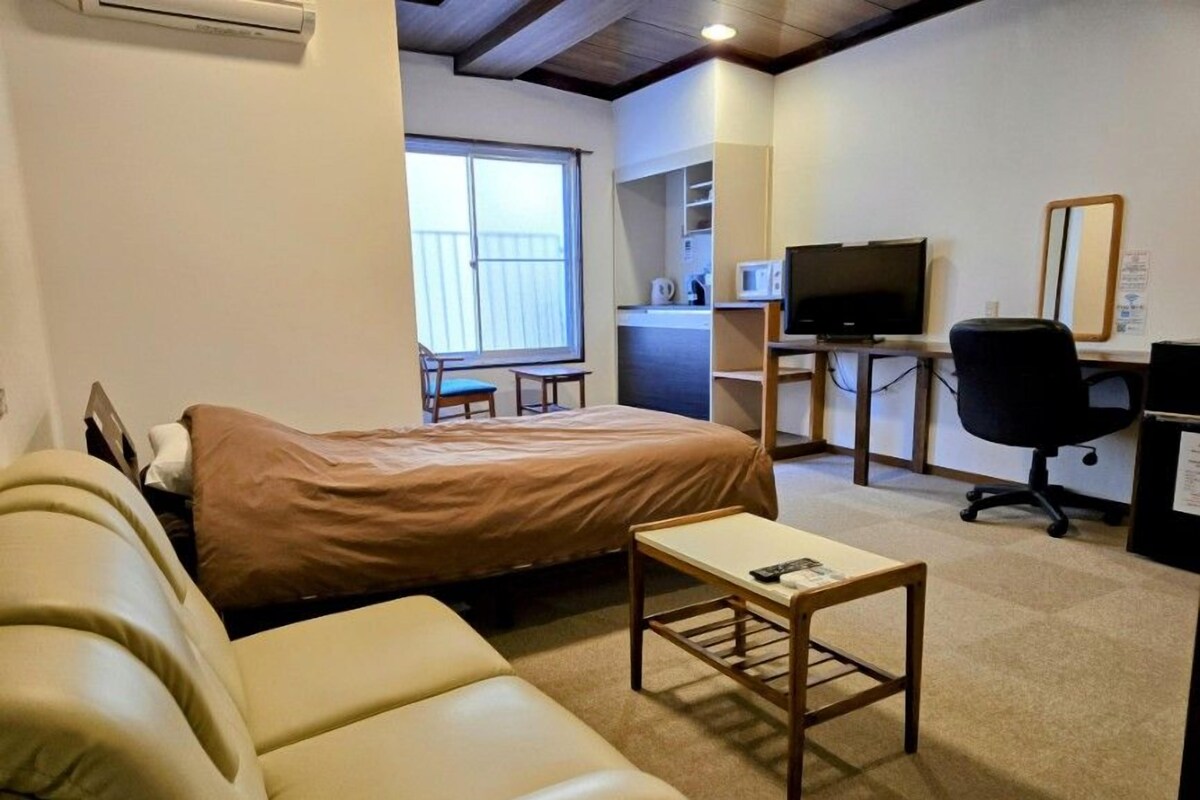Une pièce comprenant un lit, une petite table, un bureau avec un ordinateur, une chaise et une fenêtre.
