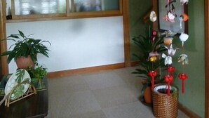 Habitación con un ventanal grande, techo de madera y pared decorada con adornos colgantes. Hay plantas en macetas en el suelo.