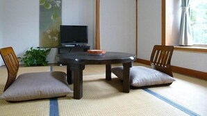 Una habitación japonesa tradicional con suelo de tatami, una mesa baja, dos cojines, un televisor y un divisor shoji.