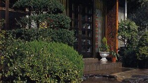 Un edificio japonés tradicional con un letrero, un vestíbulo cubierto y un jardín bien cuidado.