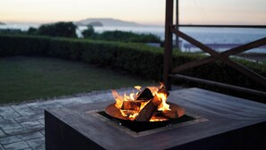 A fire pit with logs burning, set on a concrete platform with a view of the sea and distant hills. - Sea Side Villa Kamano (Takamatsu)