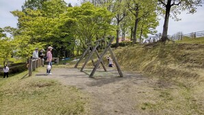 A playground with swings and a fenced area, surrounded by trees and a grassy hill. - Kanaya Onsen Hotel Ginga Park Hanamaki (Hanamaki)