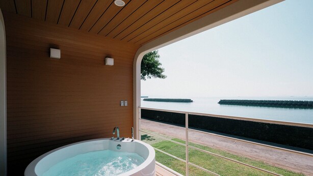 A bathroom with a large bathtub, wooden ceiling, and a view of the sea through a glass door. - Thousand Garden Tarumizu (Tarumizu)