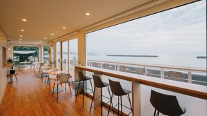 A modern interior with a long balcony overlooking a body of water, featuring a seating area with chairs and tables. - Thousand Garden Tarumizu (Tarumizu)