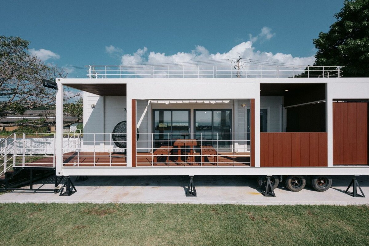 Una casa móvil moderna, de color blanco, con una terraza grande, zona de comedor y garaje.