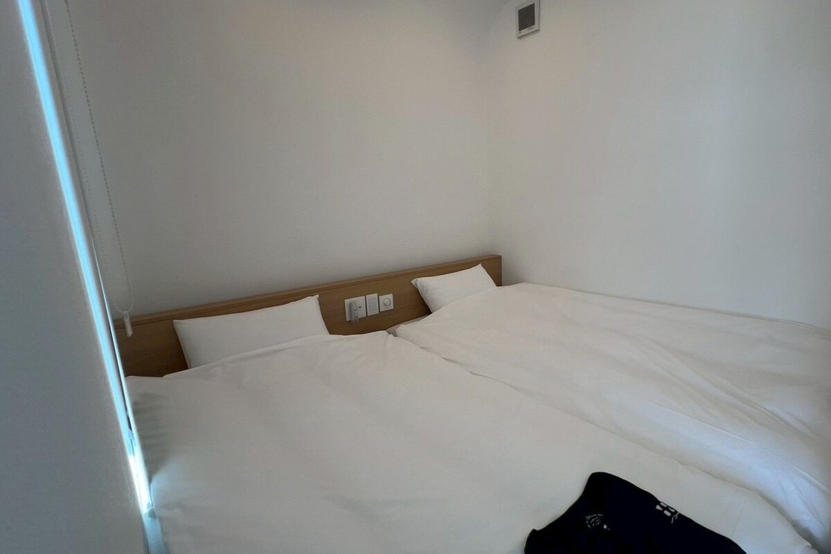 Une chambre d’hôtel simple et sans fioritures, avec un lit simple, une tête de lit en bois et une petite fenêtre.