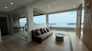 A modern living room with a sofa, a small round table, and a view of the sea through large windows. - Thousand Garden Tarumizu (Tarumizu)