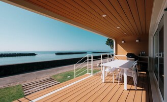 A covered outdoor area with a wooden deck, a table and chairs, and a view of the sea.