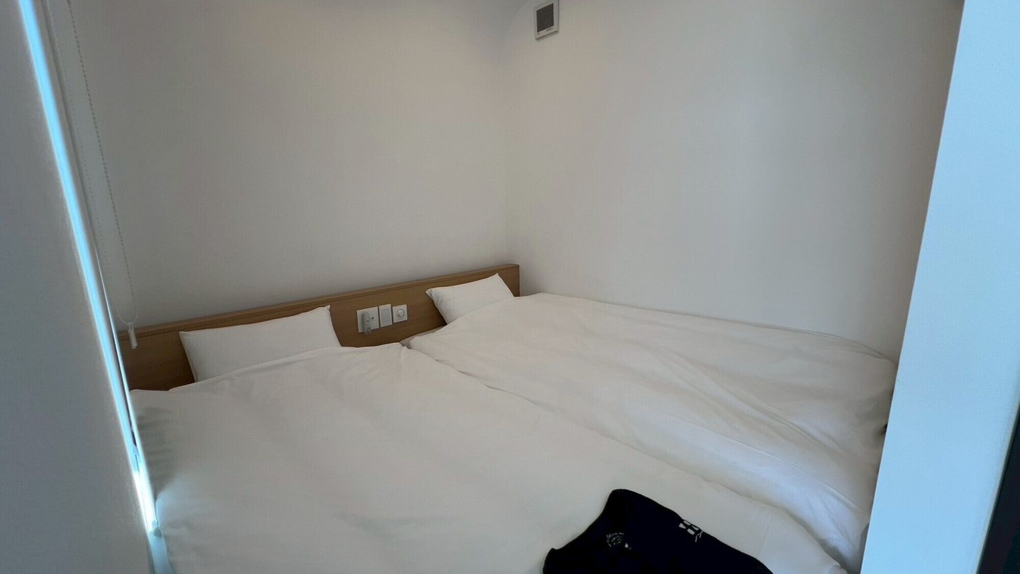 Habitación de hotel sencilla y sin adornos, con una cama individual, cabecera de madera y una ventana pequeña.