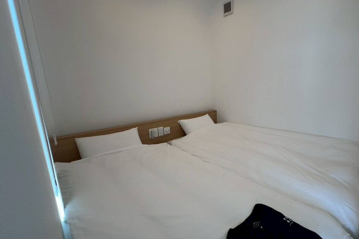Habitación de hotel sencilla y sin adornos, con una cama individual, cabecera de madera y una ventana pequeña.
