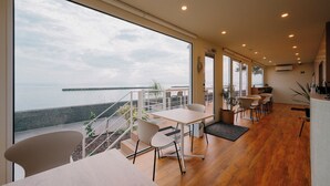 A modern interior with large windows overlooking a body of water, wooden flooring, and a seating area with tables and chairs. - Thousand Garden Tarumizu (Tarumizu)