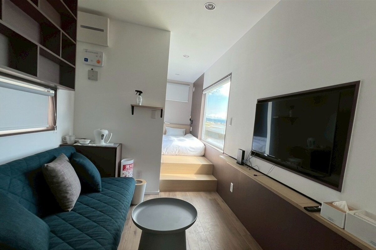 Una habitación de hotel compacta con una cama, un televisor, un sofá y una pequeña mesa.