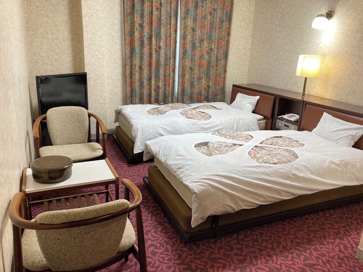 Ein Hotelzimmer mit zwei Betten, einem Schreibtisch, einem Stuhl, einer Lampe und einem Telefon.