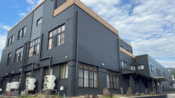 Un edificio moderno con fachada oscura, numerosas ventanas y tejado plano.