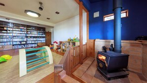 A library with bookshelves, a children's play area, and a wood-burning stove. - Kids Pension Maple (Hokuto)