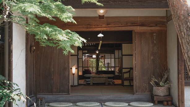 Ein traditioneller Holzeingang mit Tatami-Matten führt zu einem Raum mit niedrigem Tisch und Stühlen.