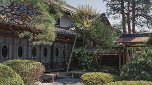 Ein traditionelles japanisches Gebäude mit einem Ziegeldach, Holzbalken und einem Kiesweg, der zu einer hölzernen Bank führt.