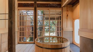 Ein traditioneller japanischer Raum mit Schiebetüren, Holzboden und einer gläsernen Onsen-Badewanne.