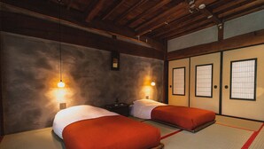 Ein traditioneller japanischer Raum mit Tatami-Matten, zwei Betten mit roter Bettwäsche und verschiebbaren Shoji-Schiebetüren.