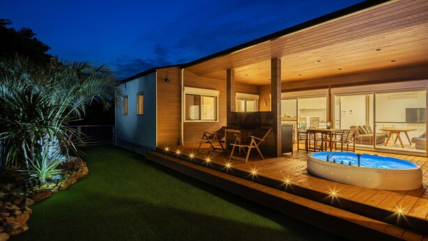 Una casa moderna con piscina, mobiliario exterior y un patio bien iluminado.