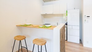 Una cocina moderna con armarios blancos, encimera de madera, dos taburetes y un refrigerador empotrado.