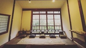 Una tradizionale stanza in stile giapponese con pavimento in tatami, un letto basso in legno, un'ampia finestra e un'anta scorrevole.
