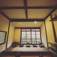 A traditional Japanese-style room with tatami flooring, a low wooden bed, a large window, and a sliding door.