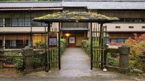 Un edificio tradizionale giapponese con un cancello in legno, una targa e un vialetto che conduce all'ingresso.