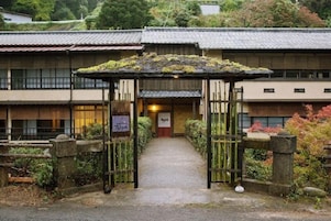 A traditional Japanese building with a wooden gate, a signboard, and a pathway leading to the entrance.