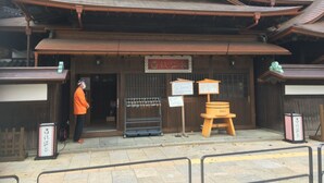 Un edifici japonès tradicional amb estructura de fusta, un cartell i una persona de peu al davant.