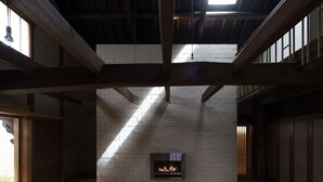 Een modern interieur met zichtbare houten balken, een metselwerk open haard en grote ramen die natuurlijk licht binnenlaten.